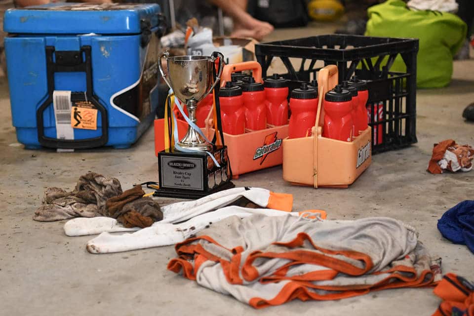 The Black & White Cabs Cup trophy sits on the floor of the Rugby league locker room after a game, amongst some orange water bottles and a blue esky